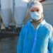 A woman wearing protective clothing, including a mask and hair net, outdoors at an industrial site.