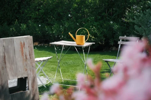 Yellow watering can on a small table in a garden.