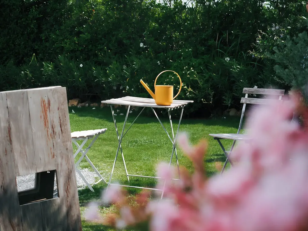 Yellow watering can on a small table in a garden.