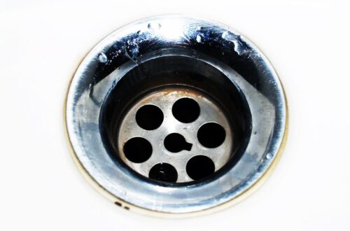 Detailed image of a chrome sink drain showcasing water droplets and a metallic finish.