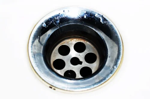 Detailed image of a chrome sink drain showcasing water droplets and a metallic finish.