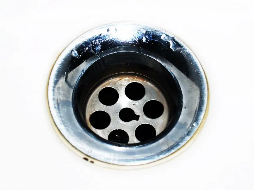 Detailed image of a chrome sink drain showcasing water droplets and a metallic finish.